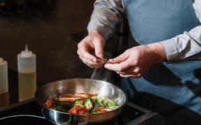 cuoco che mette origano in una padella con verdure